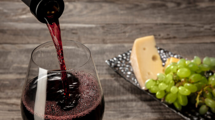 Delicisious and tasty food and drink. A bottle and a glass of red wine with fruits over weathered wooden background. Top view with copy space to insert your text or image for ad. Grape and cheeseplate.